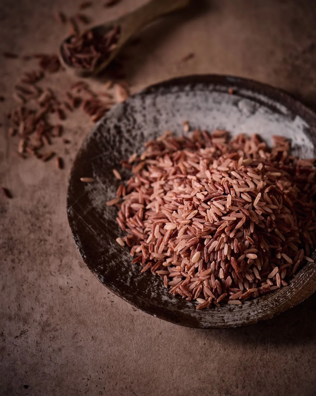 flatlay image of raw red rice in moody brown hued scene