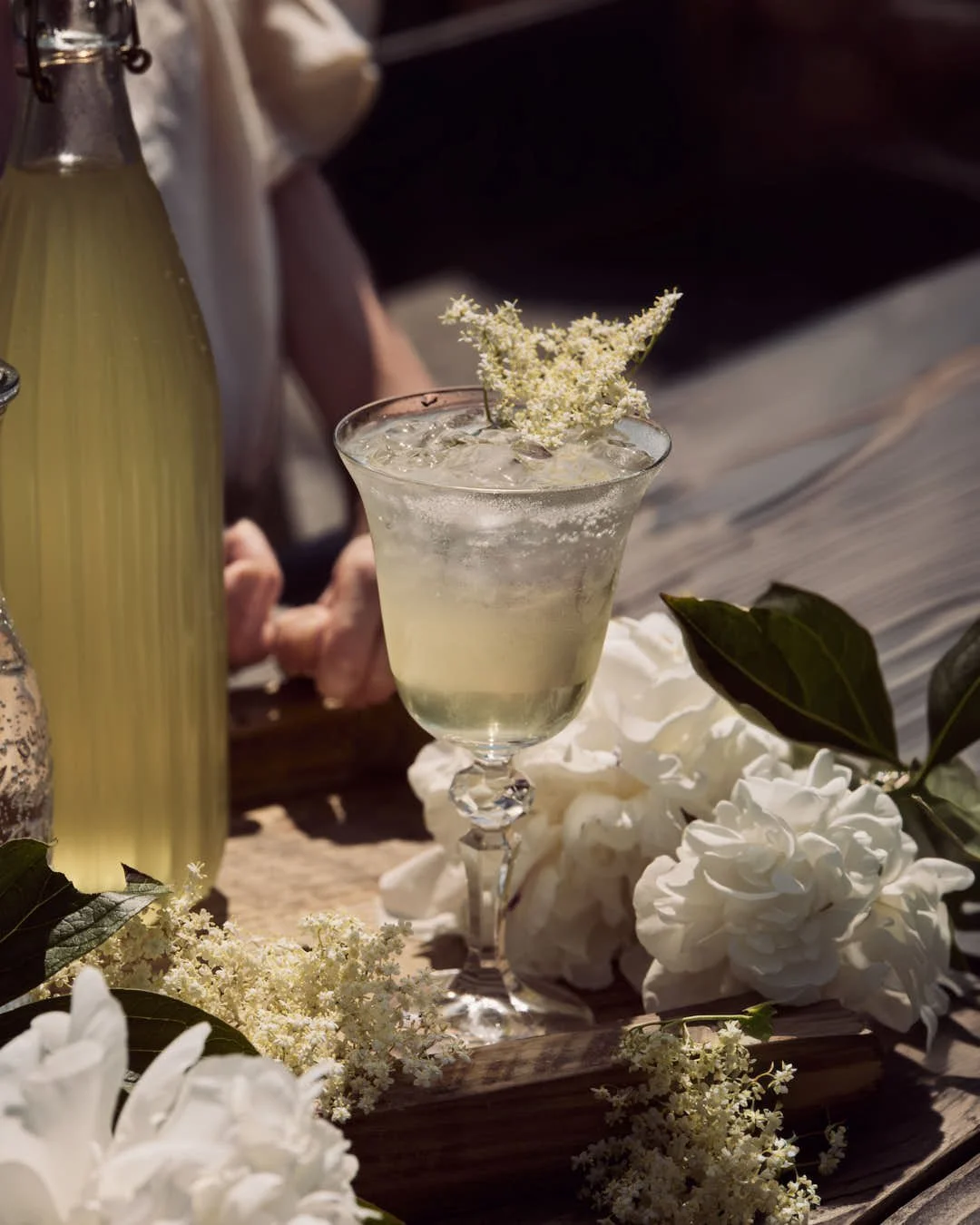straight on image of girl enjoying elderflower codrial in glass on rustic outdoor table