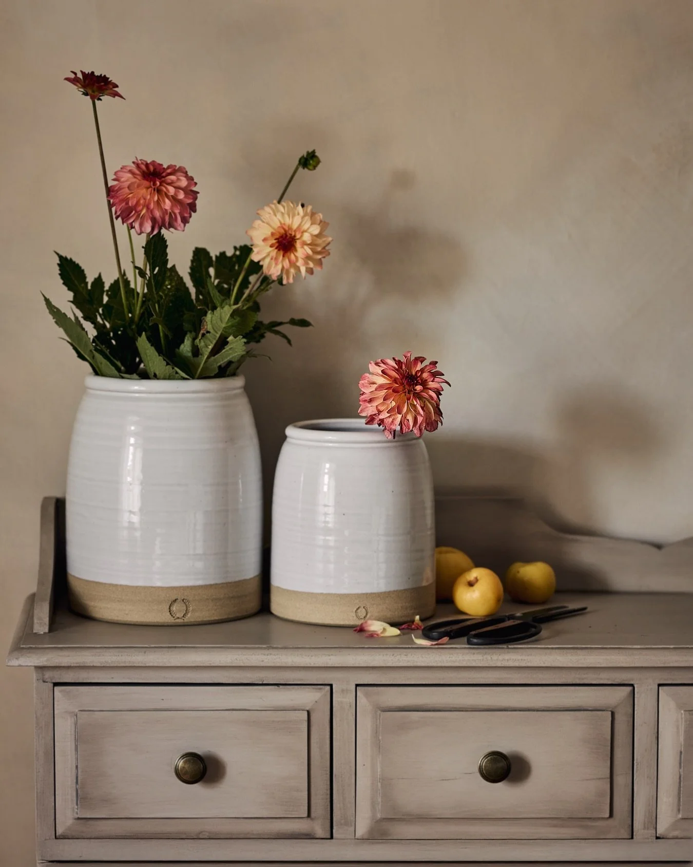 Two crocks, quietly holding the season&rsquo;s last dahlias &amp; Quince&mdash; petals blushing with the warmth of summer&rsquo;s farewell. A still moment where beauty lingers, softly fading into autumn&rsquo;s embrace.

Crocks @farmhousepottery 
Dah