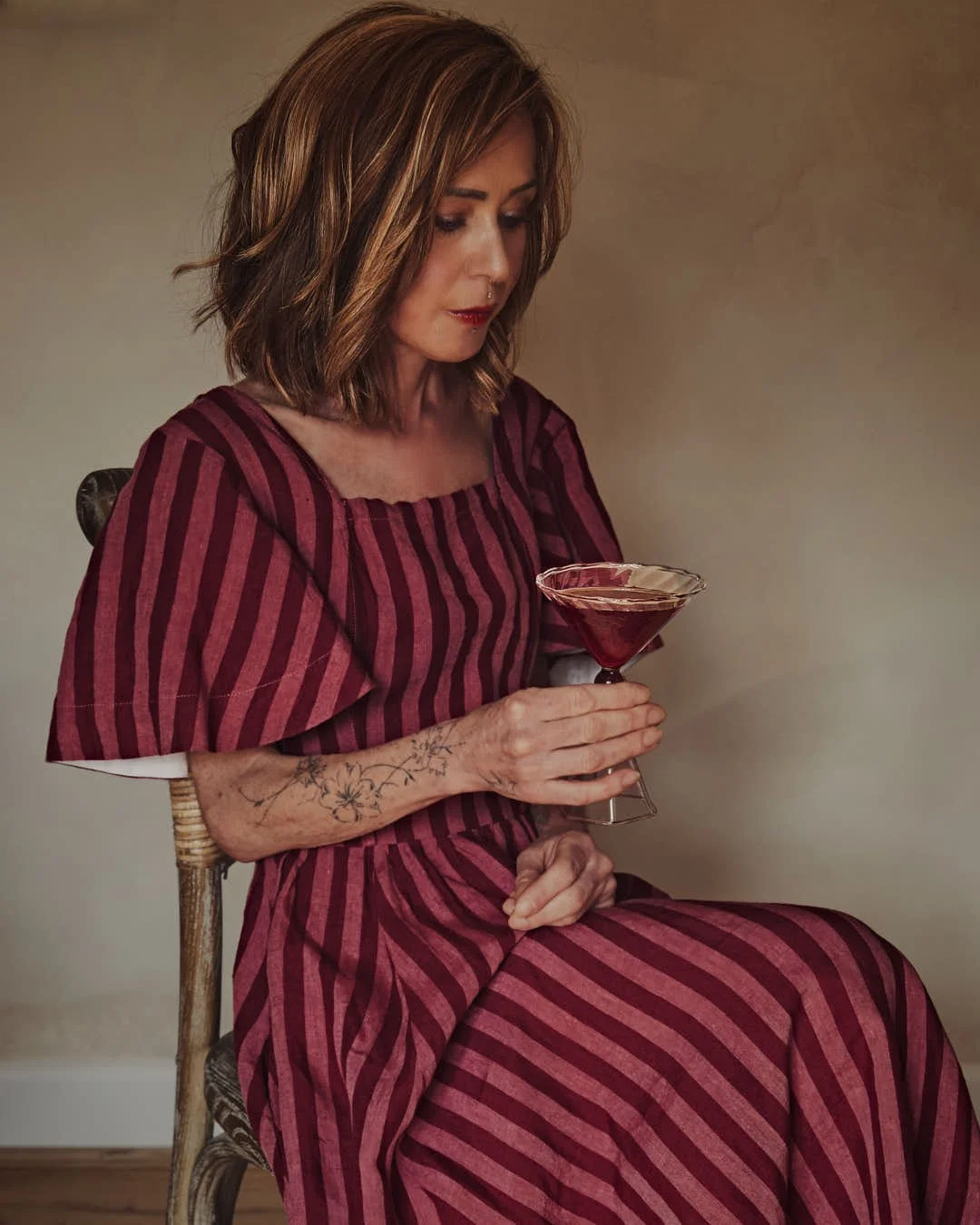 girl in pink and red striped dress sittin on chair contemplating red hued martini in stunning image