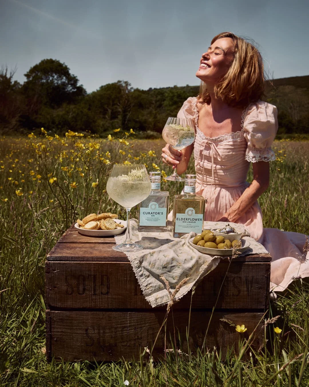 straight on image of girl enjoying spritz in summer meadow by picnic