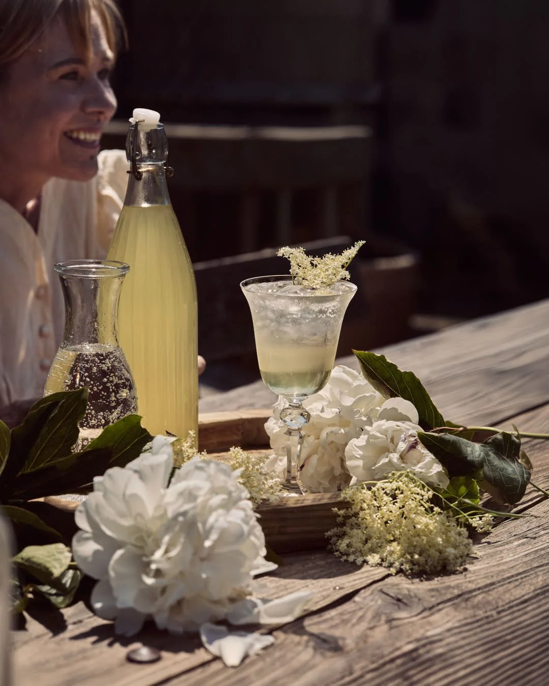 straight on image of girl enjoying elderflower codrial in glass on rustic ourtdoor table