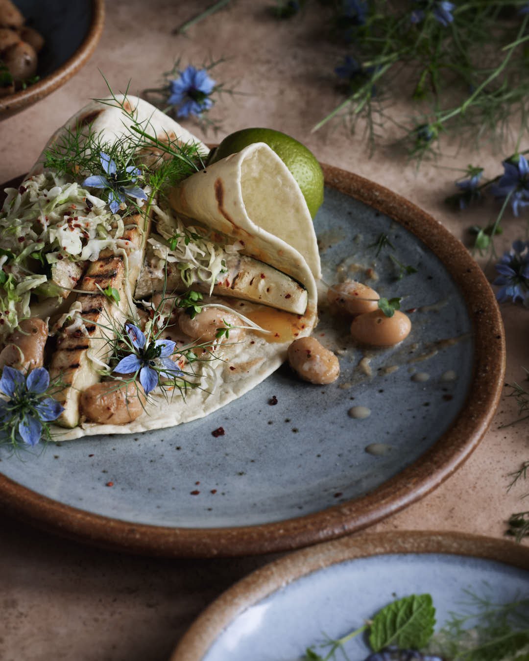 angled image of folded flatbread with courgette spears and edible flowers with beans and herbs