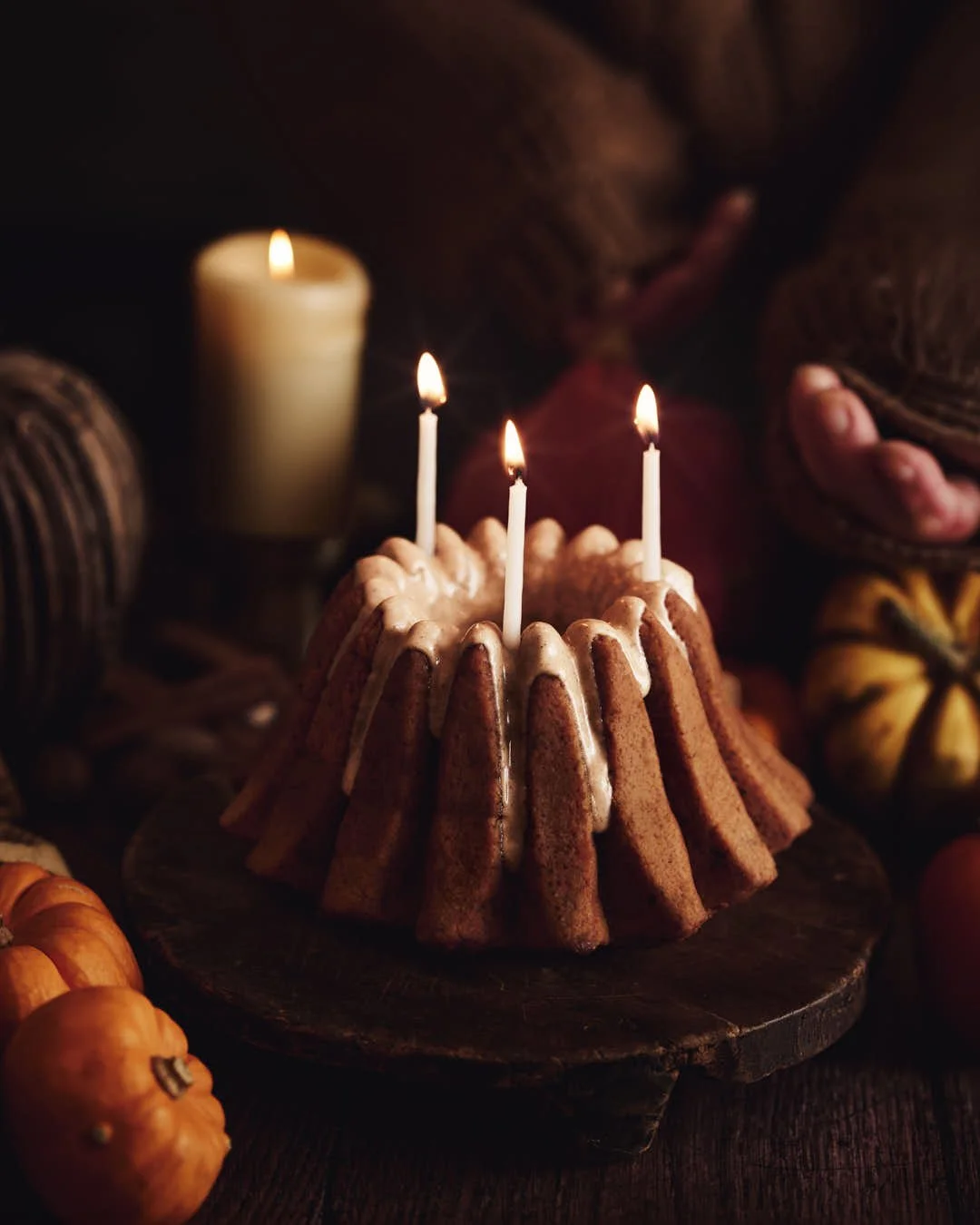 angled macro image of bundt cake with glaze drizzle and candles in dark moody scene