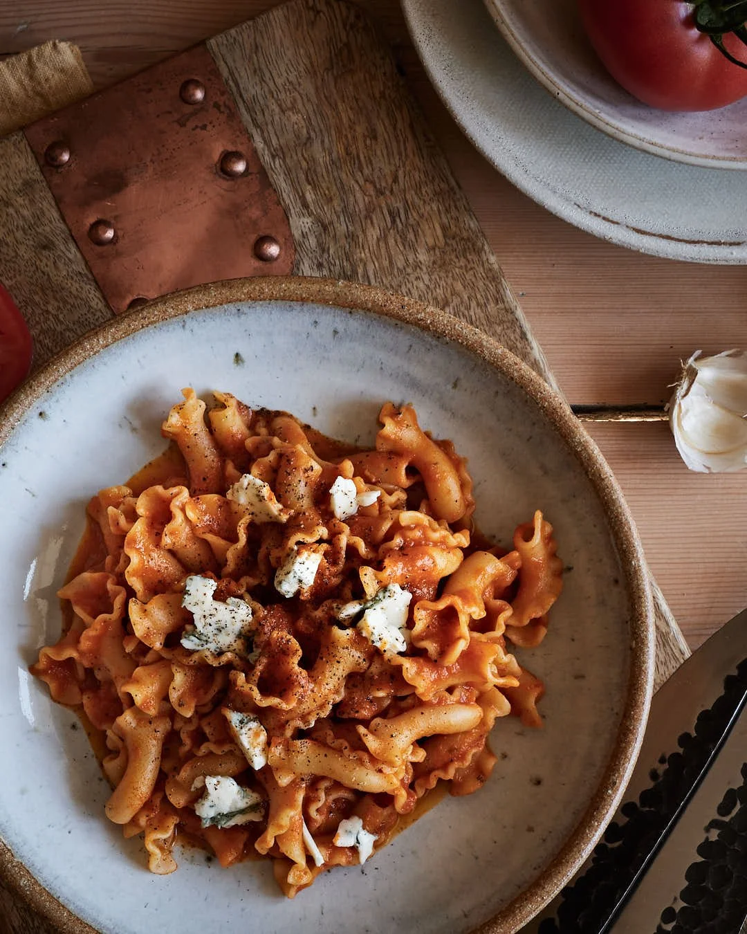 bowl of fresh tomato pasta in warm sunlit flatlay with doclelatte and rustic wood and tomatoes surrounding