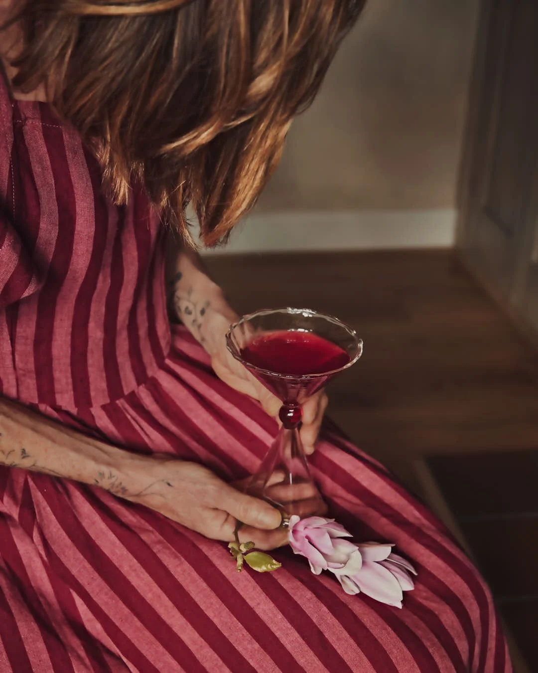 macro shot of girl leaning over martini in red and pink hued dress in vintage scene
