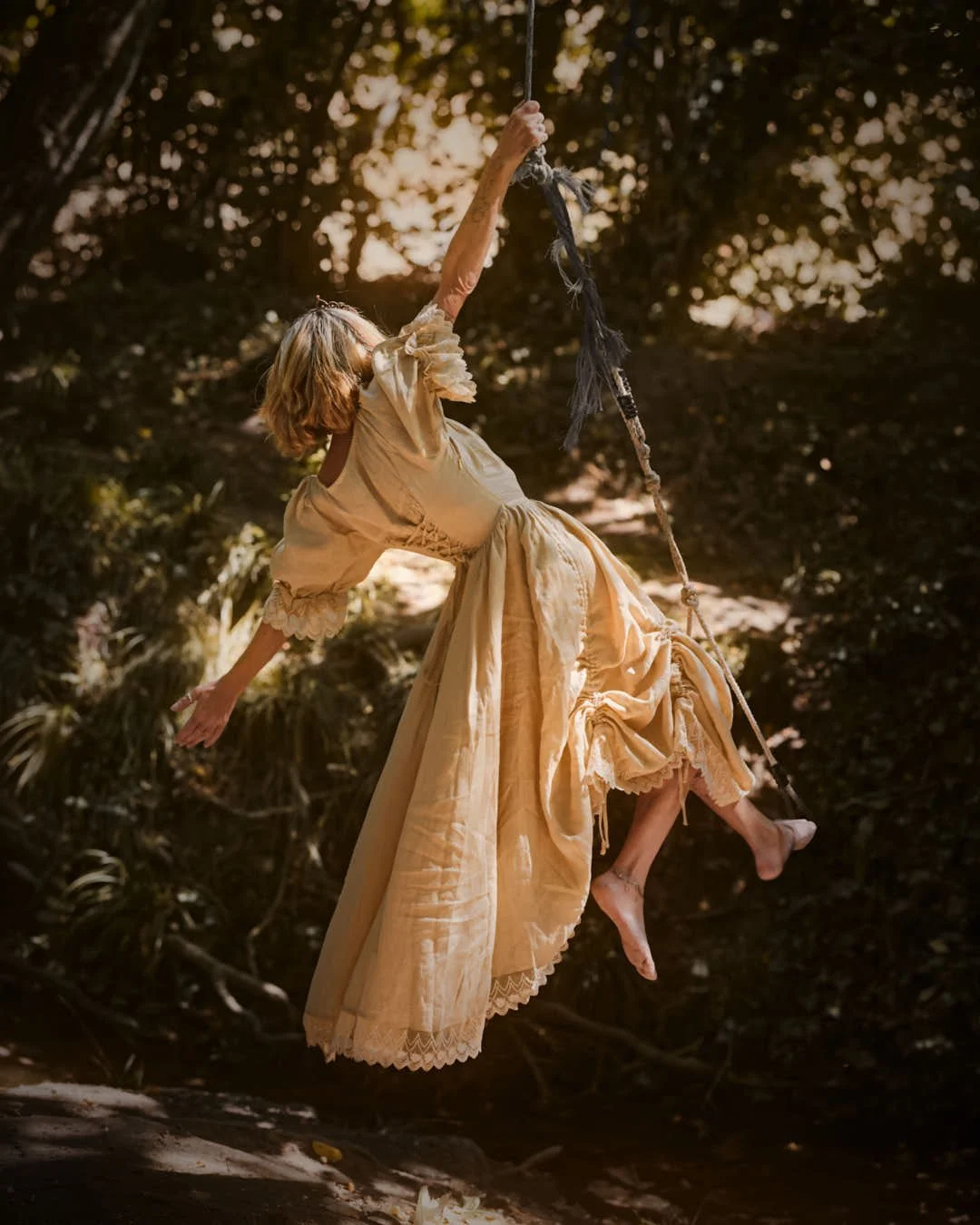 girl swinging on rope in vintage dress in woodland