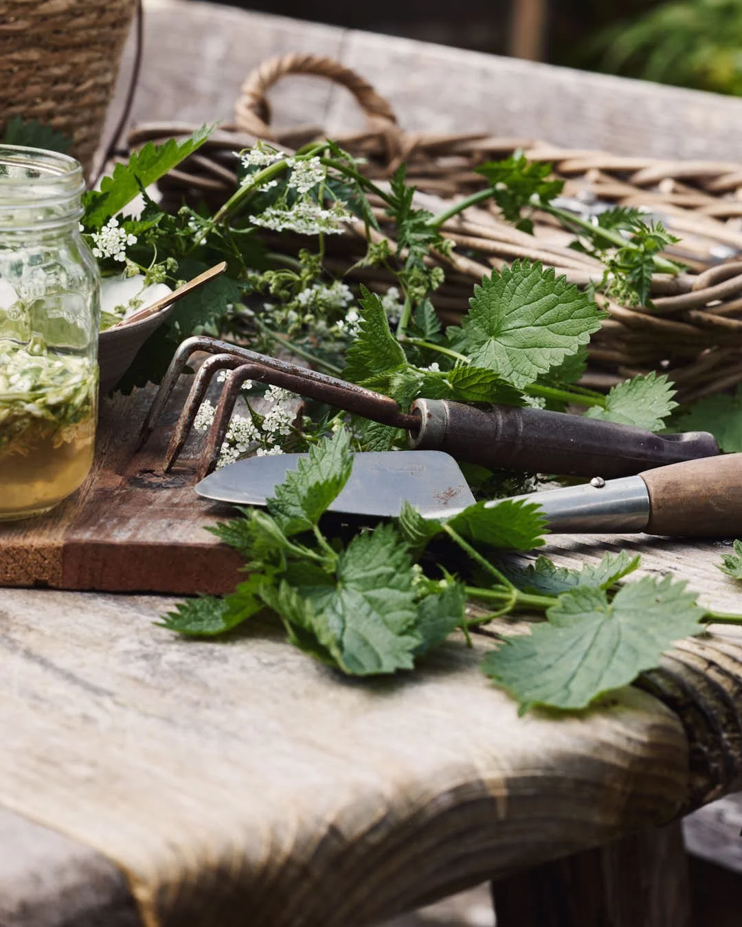 angled image of garden implements and nettles atop wooden table in gardening scene