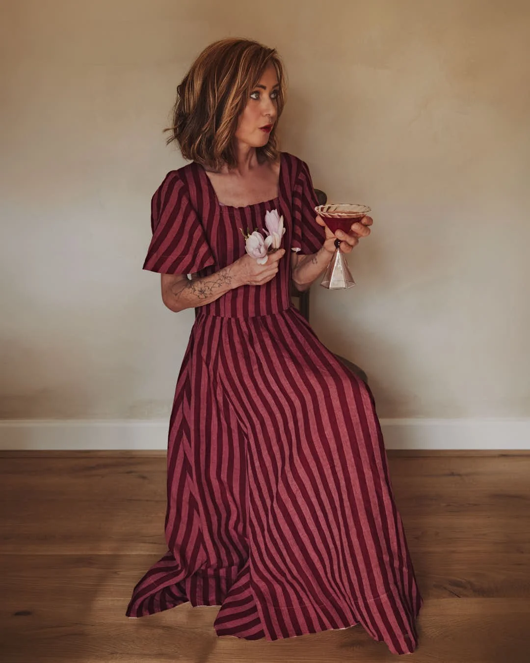 girl looking perplexed on chair holding pink hued martini and magnolia flowers in stunning image