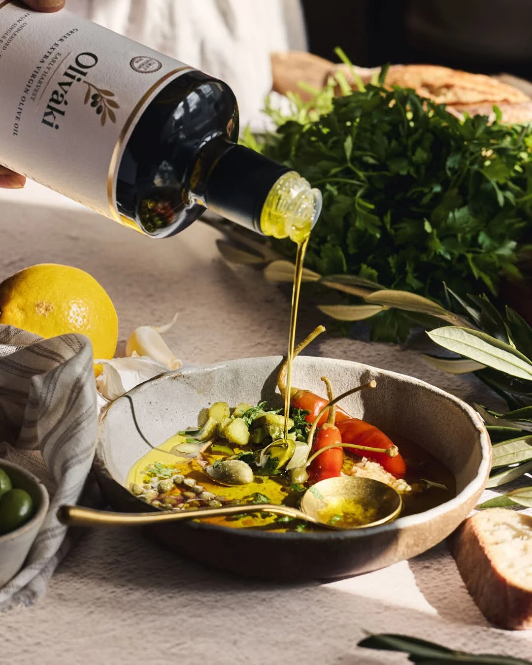 olive oil being poured into dish over herbs, chillies and garlic in sunlit scene