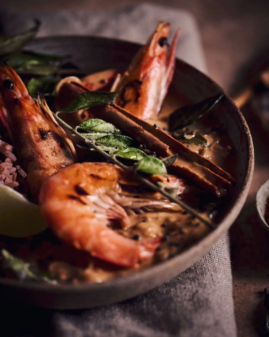 angled macro image of king prawns in curry sauce with toasted curry leaves in dark and moody scene