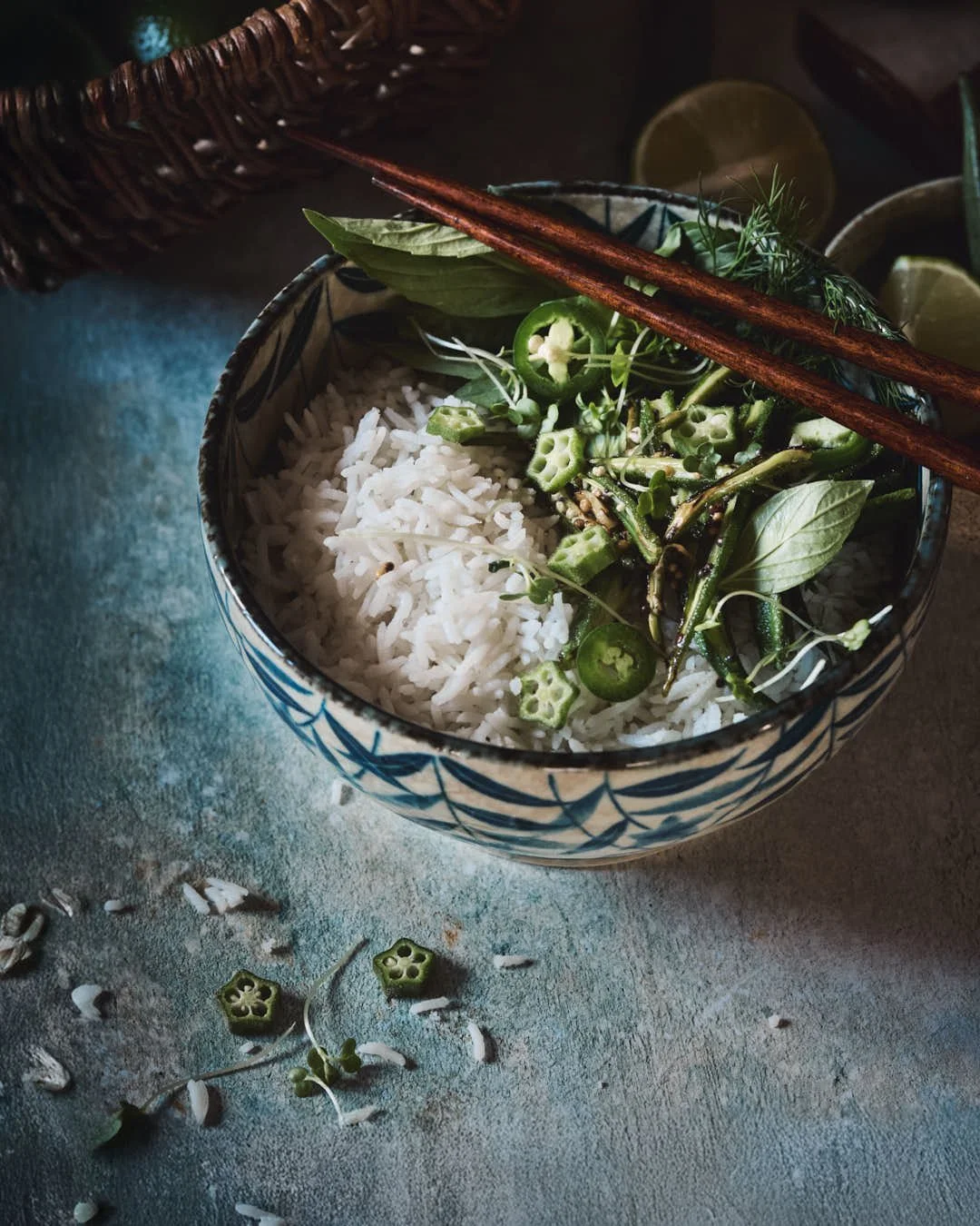 angled image of mottled blue backdrop with a asian inspired bowl of rice and okra with chillis
