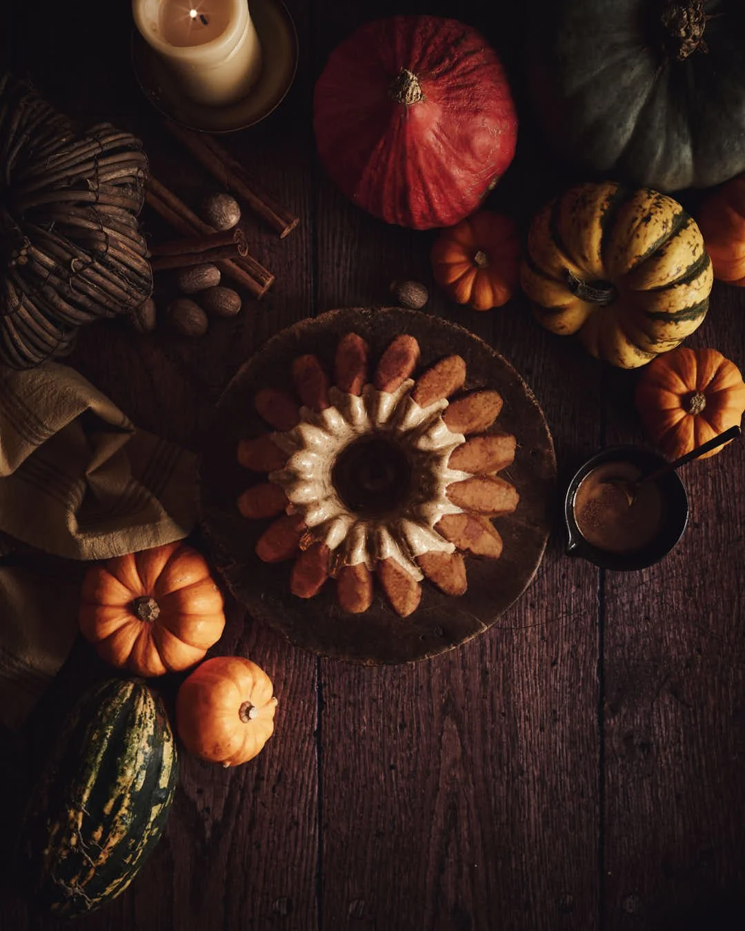 flatlay image of fluted bundt cake surrounded by pupkins on wooden table in moody scene