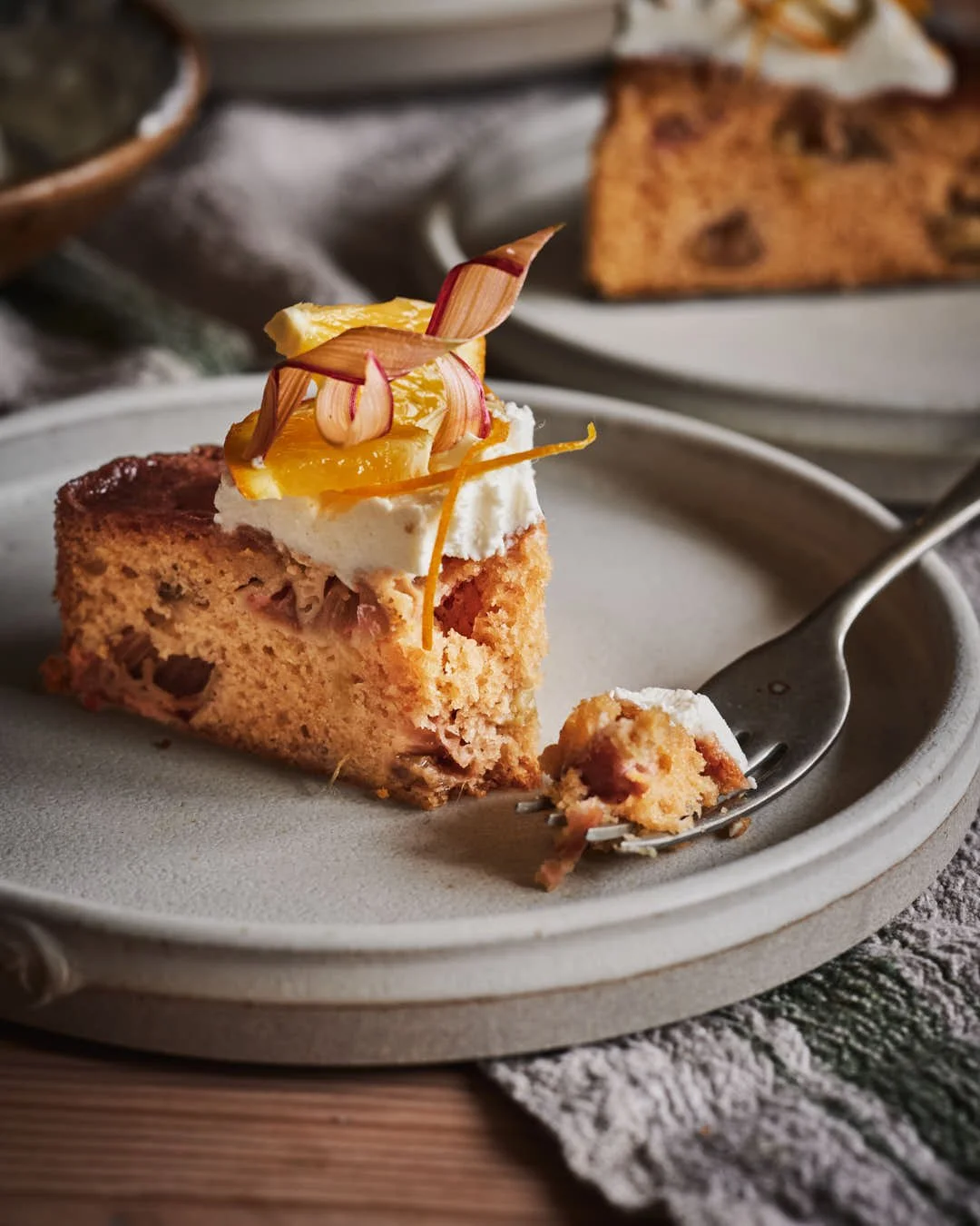angled image of slice of cake with mascarpone, orange and rhubarb curl garnish