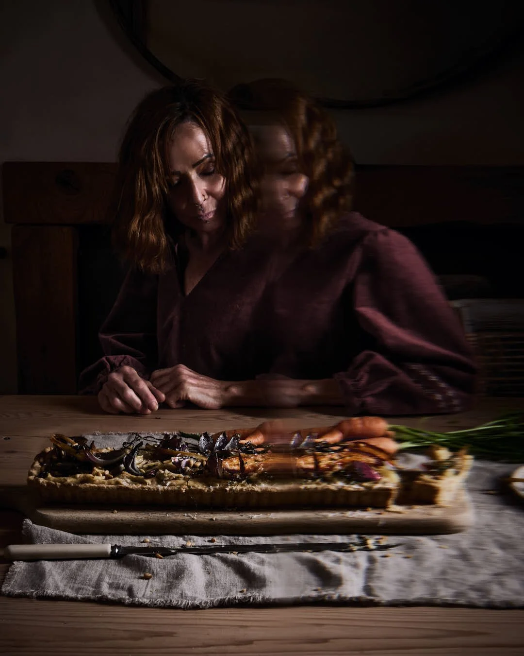 straight on image of girl sitting at kitchen table contemplating tart with blur to right in moody ghostly scene