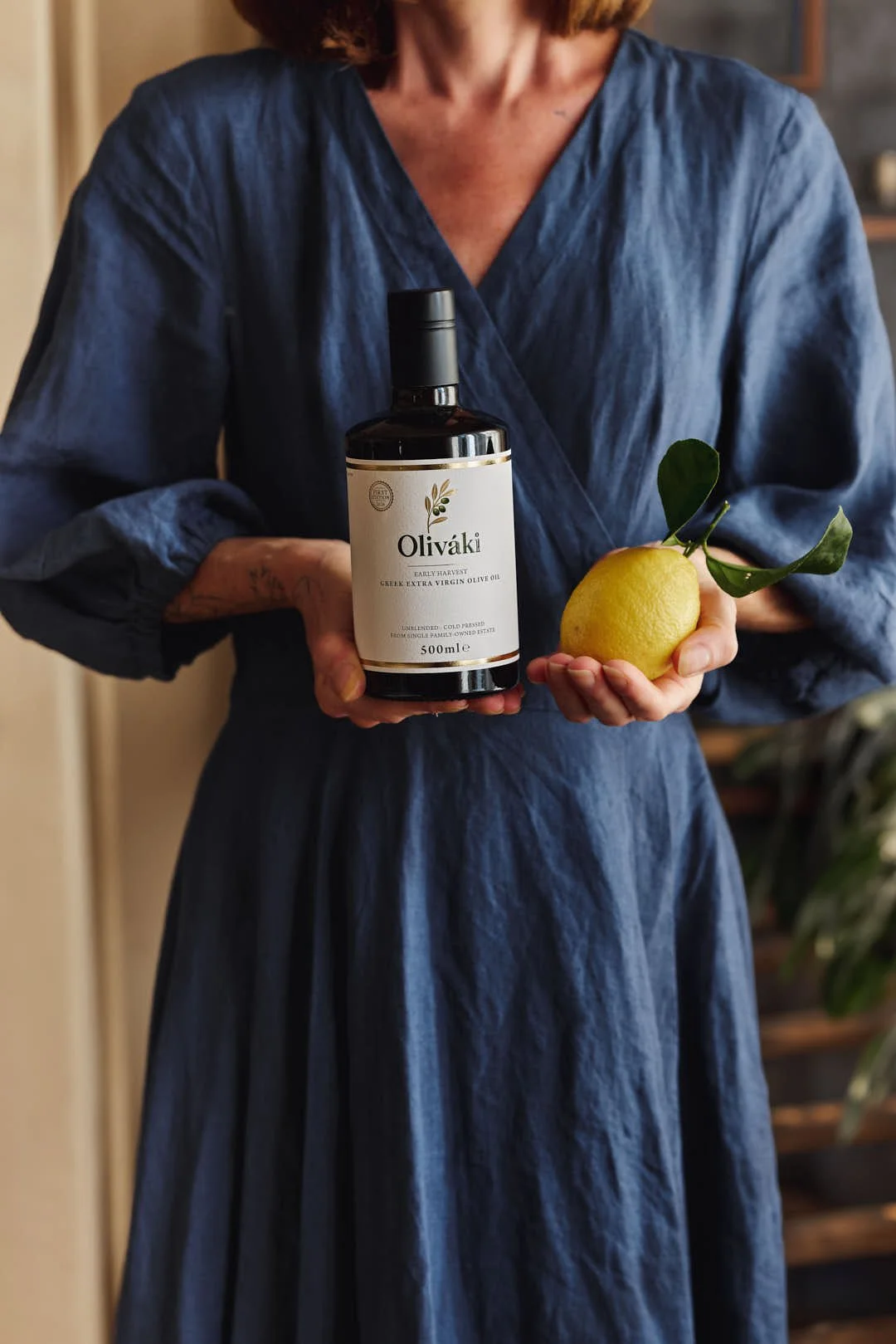 straight on image of girl holding olive oil and lemon in blue dress