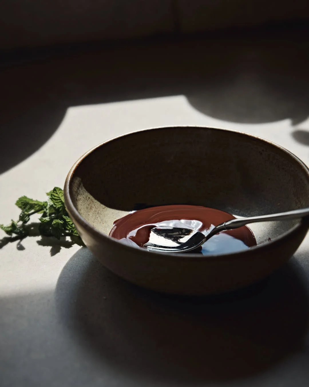 bowl with melted chocolate in stunning backlight with silver spoon and fresh mint