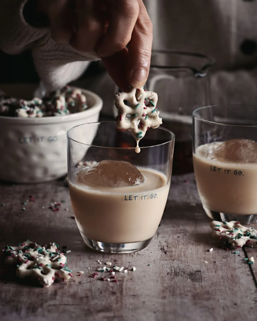 girl's hand lifting white chocolate pretzel from glass of rum cream in winter scene on worn wood kitchen table