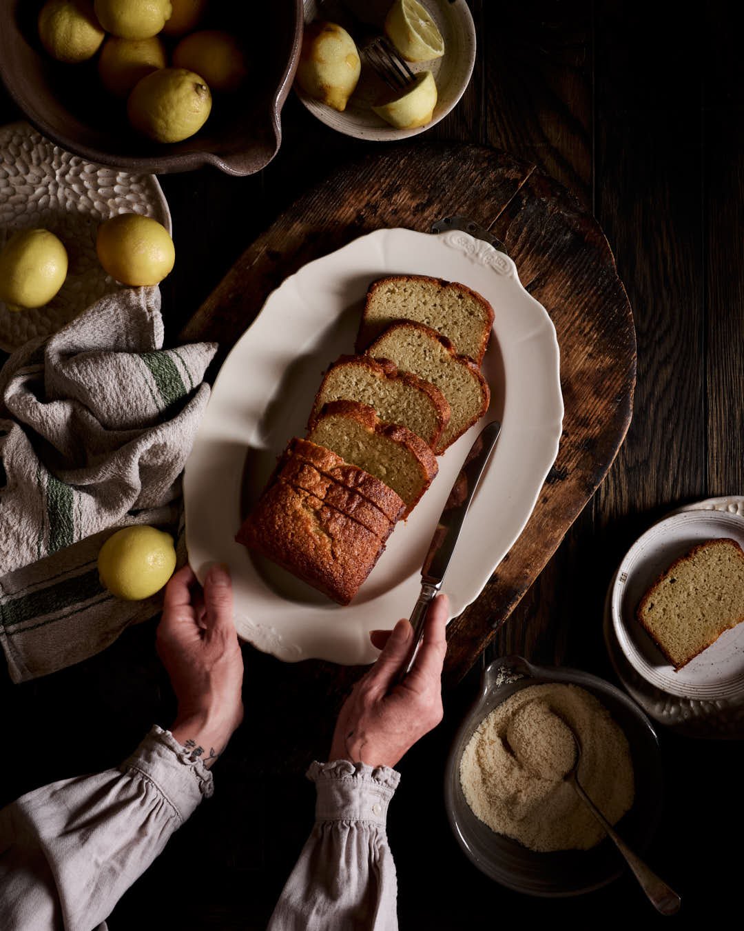 flatlay image of girls hands reaching for sliced lemon loaf cake in dark moody scene