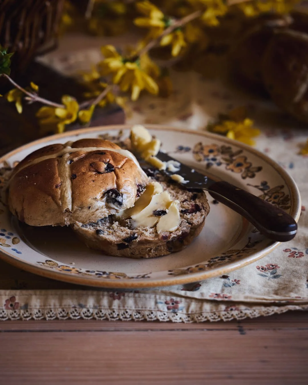 angled macro image of hot cross bun cut open to show fruit and butter