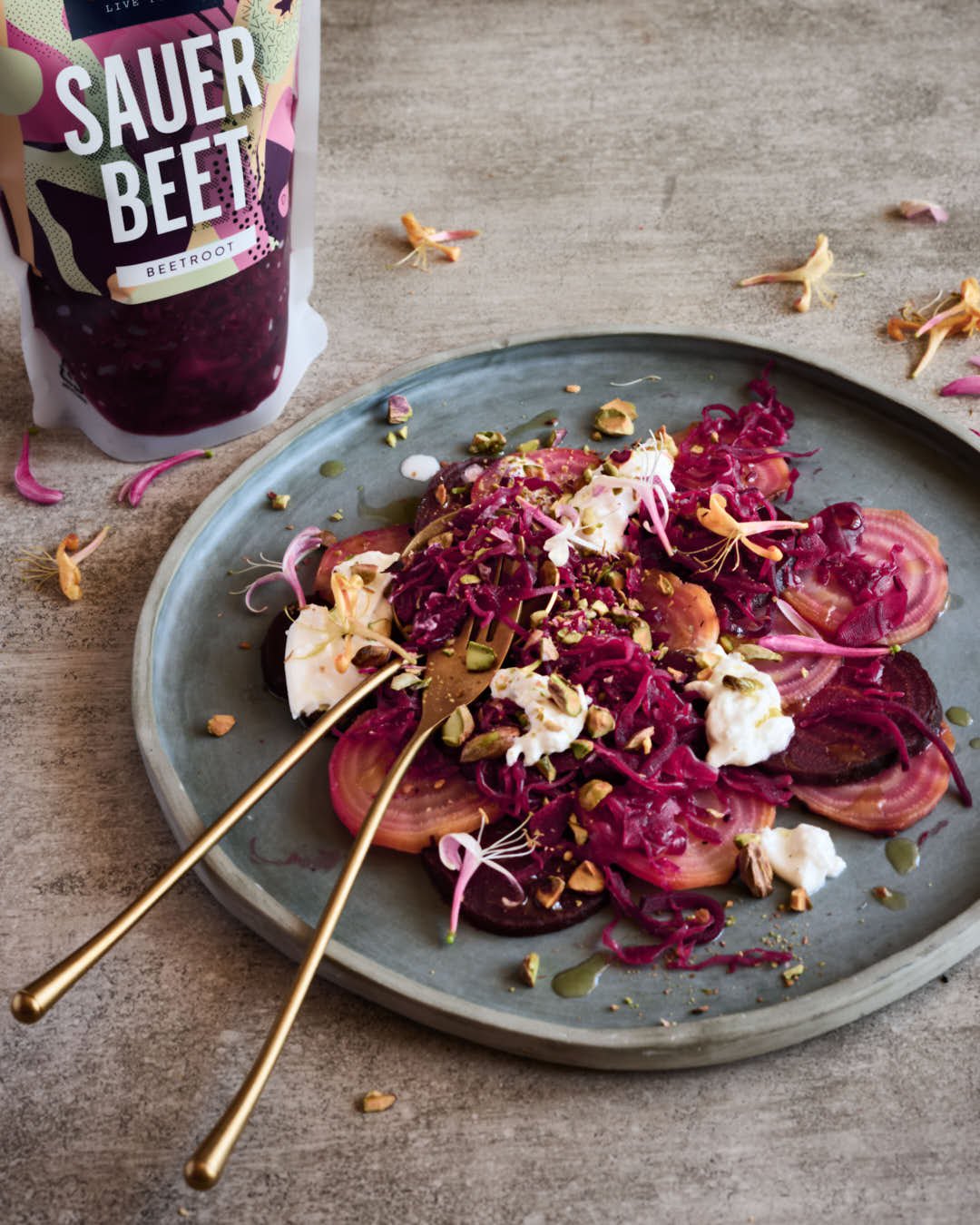 angled image of beet salad with burrata and pistachio texture in bright scene with bag of beet kraut to back