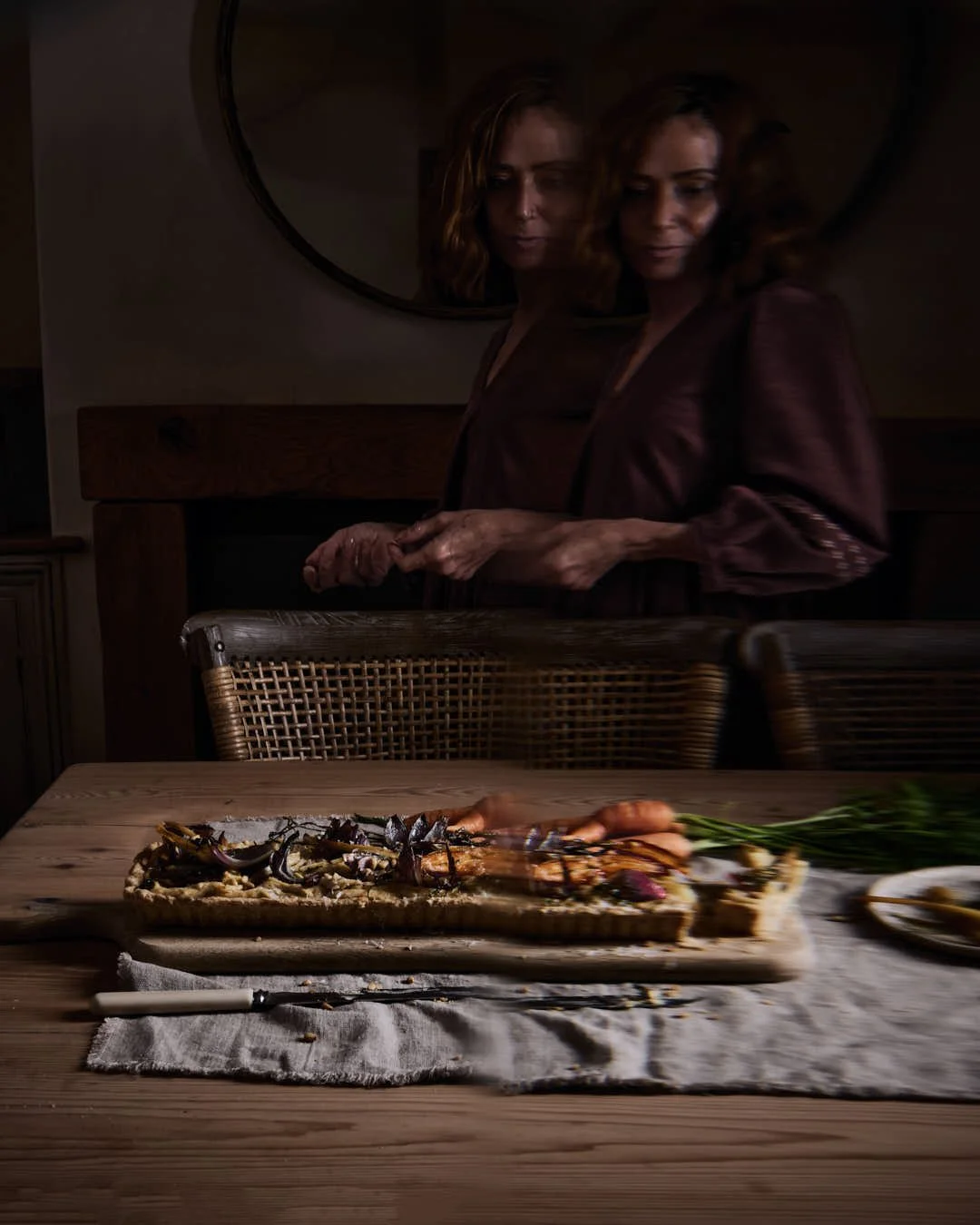 straight on image of ghostly girl walking behind table with roasted root tart in dark and moody scene