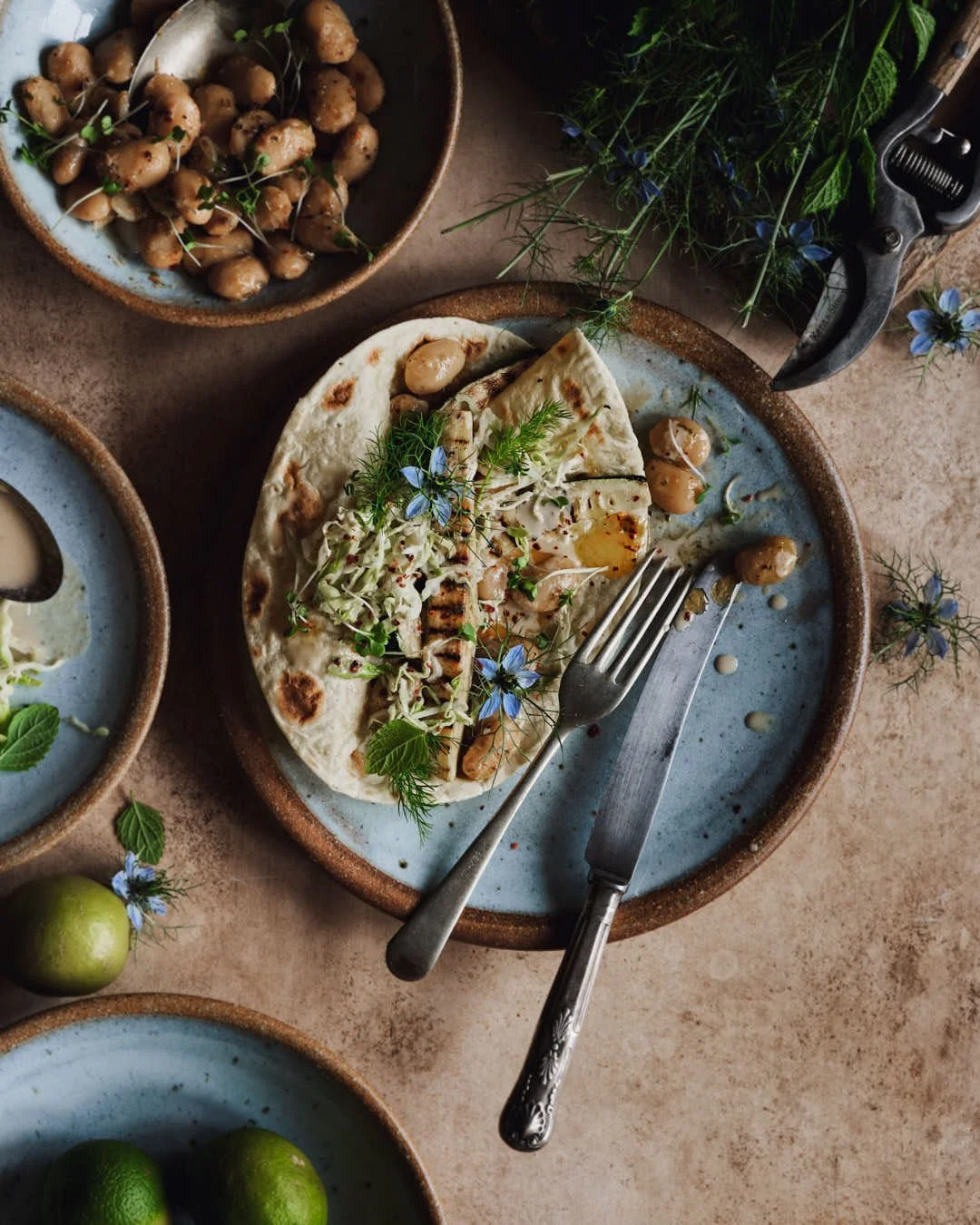 flatlay image of folded flatbread with courgette spears and edible flowers with beans and herbs