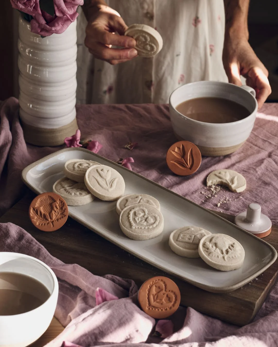 angled image of platter of stamped cookies on pink tablecloth with girls hands reaching for cup of tea in stunning vintage scene