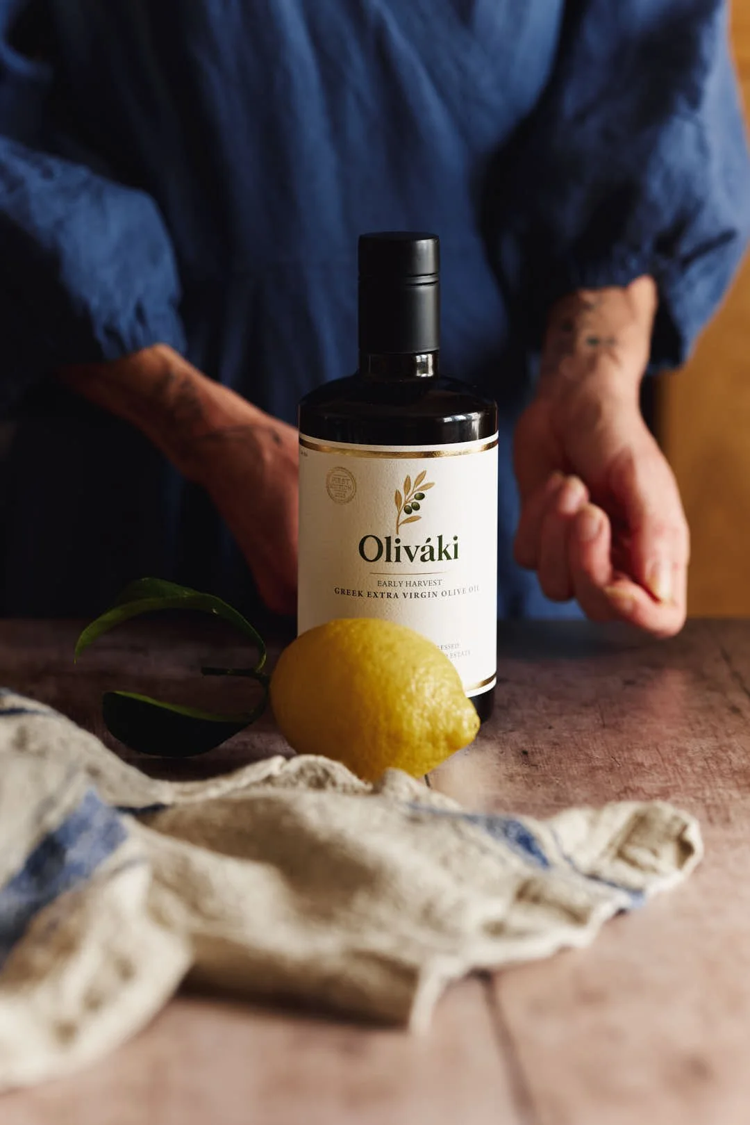 girl reaching for olive oil by lemon on rustic wood surface with cloth