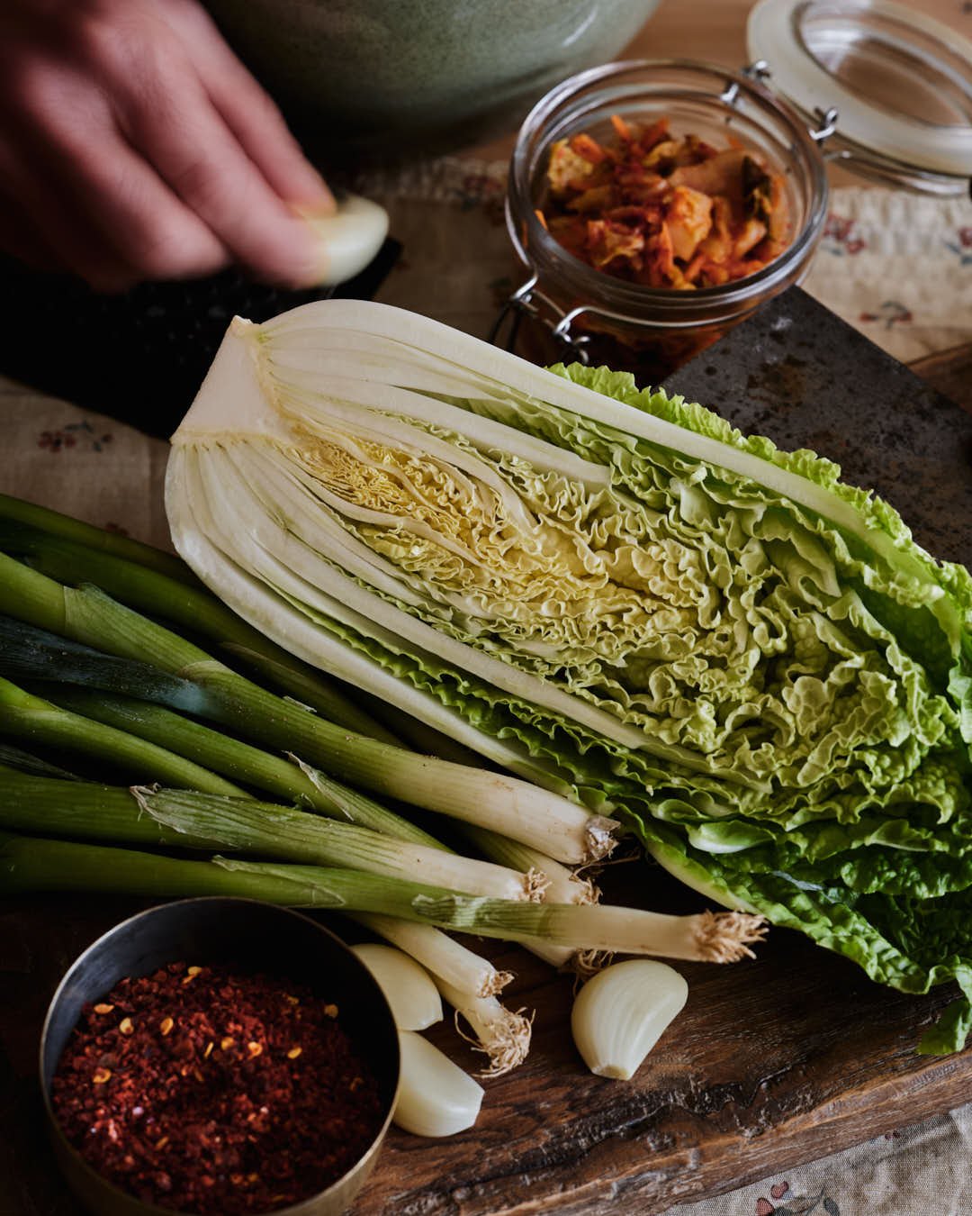 macro image of chinese leaf on chopping board surrounded by spring onions, garlic and dried chilies, fast movement of hand grating garlic to back