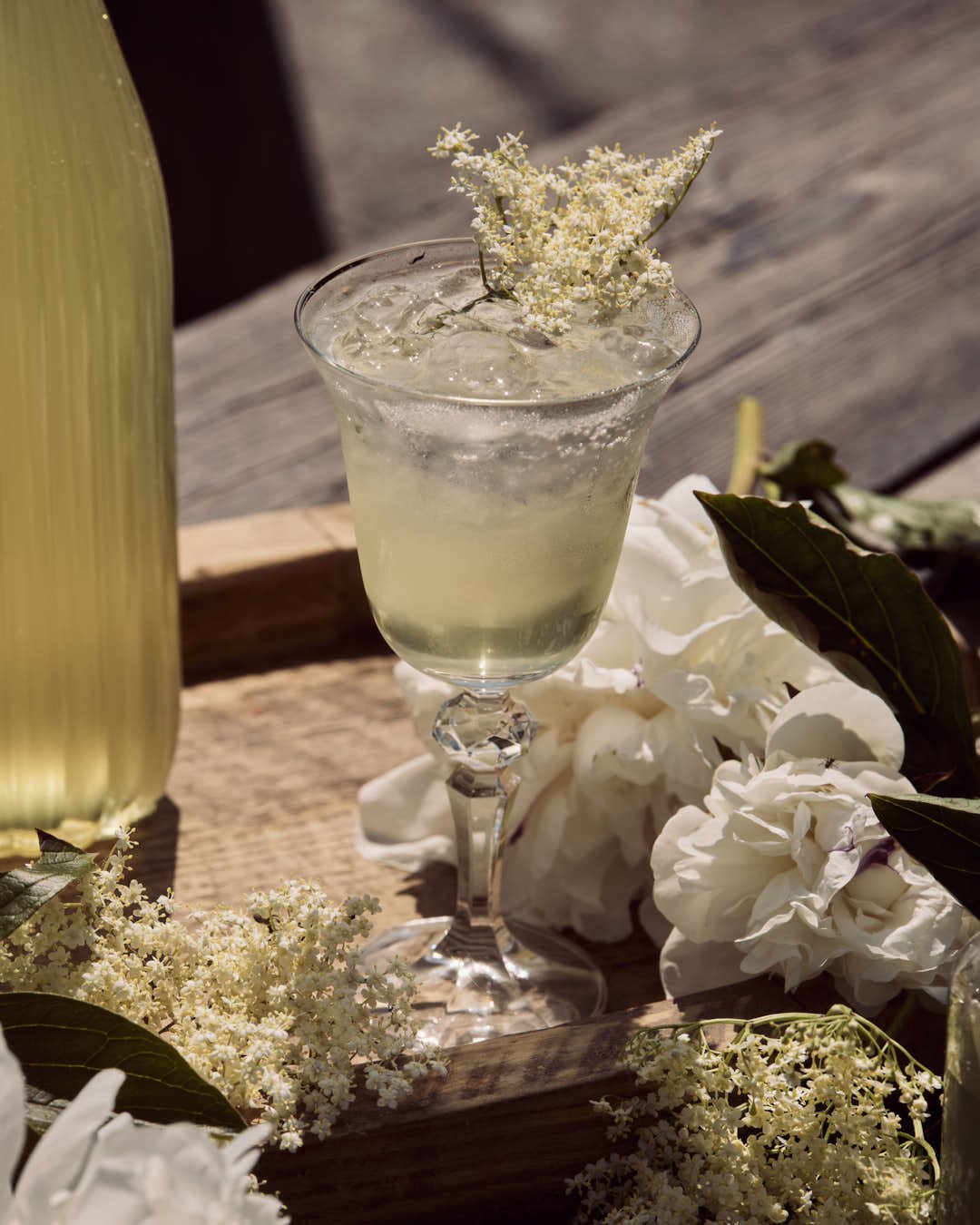 straight on image of girl enjoying elderflower cordial in glass on rustic ourtdoor table