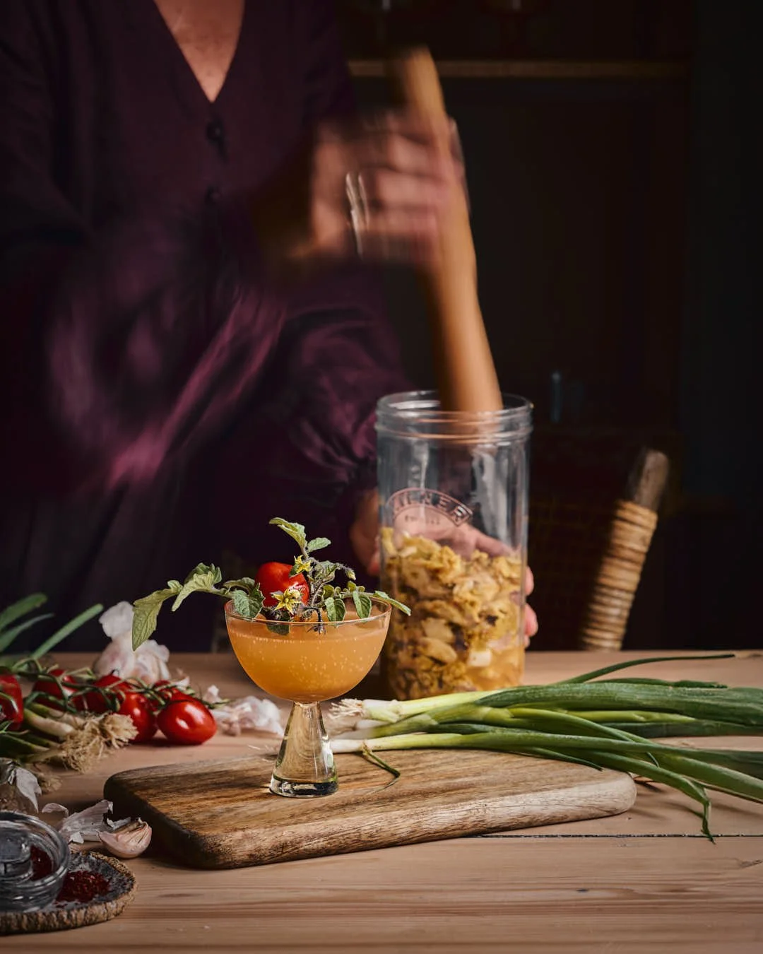 angled straight on image of glass of martini garnished with tomato leaves and tomato in rustic farmhouse scene