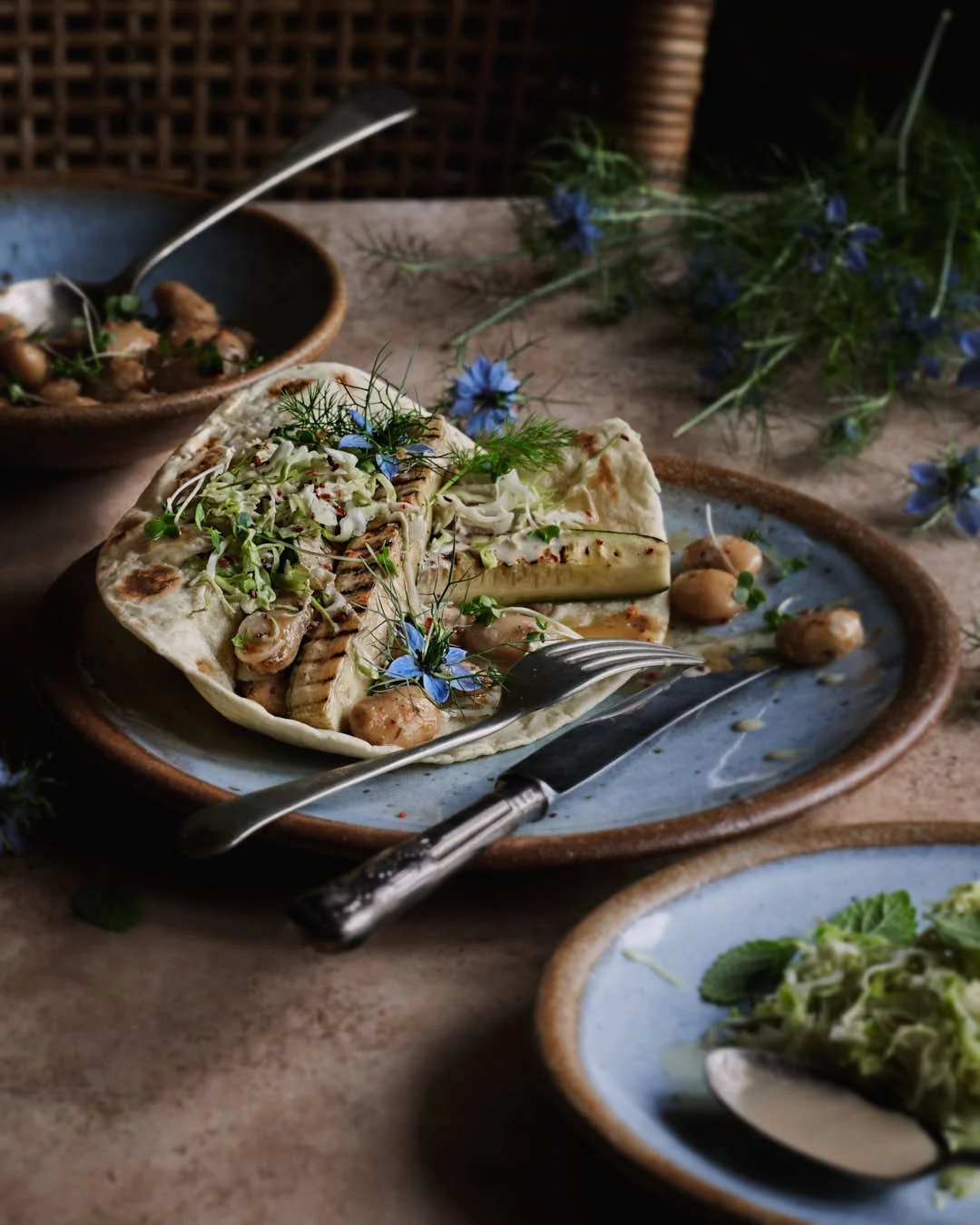 angled image of folded flatbread with courgette spears and edible flowers with beans and herbs