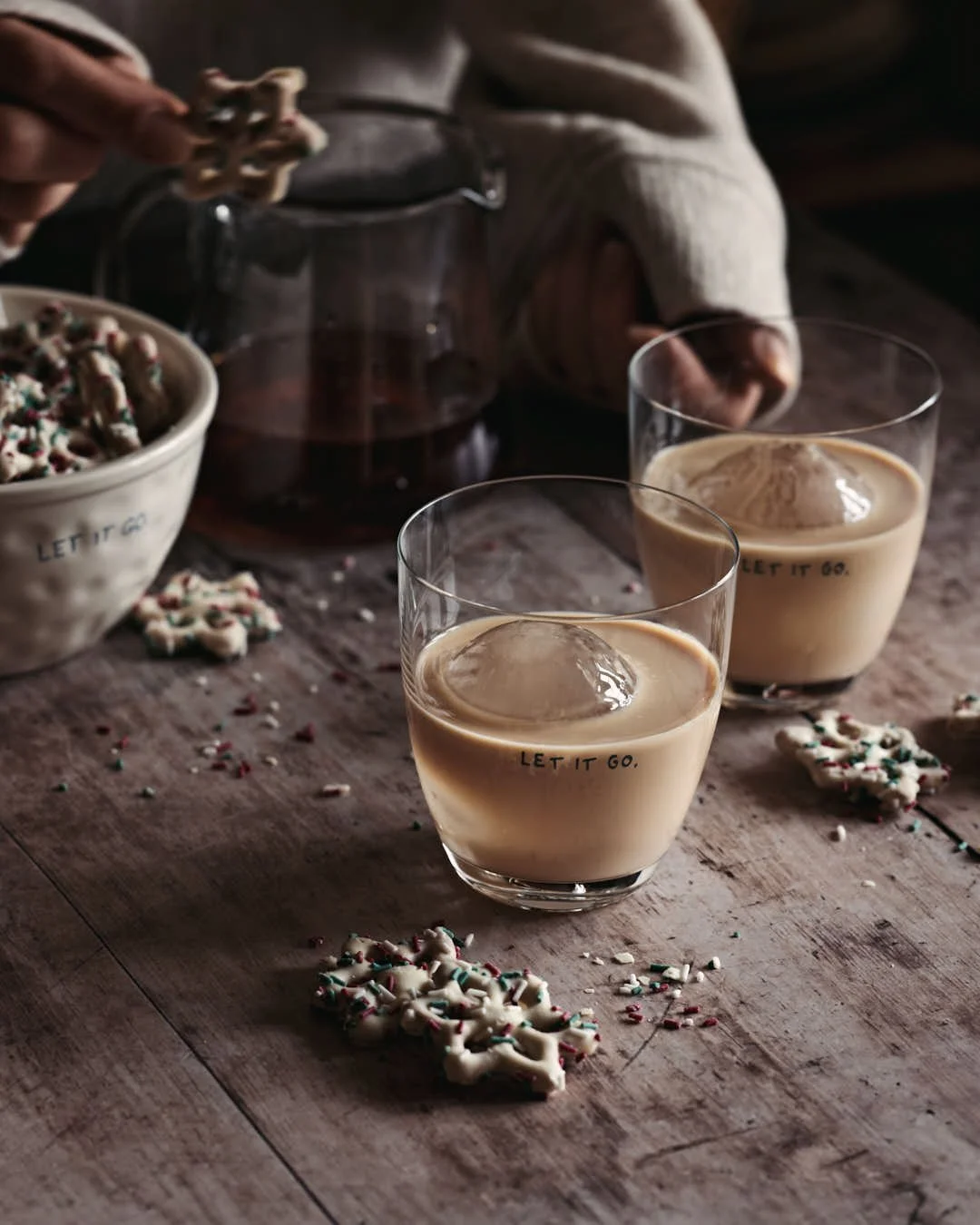 angled image of girl reachin for glass of rum cream in festive winter scene with white chocolate pretzels