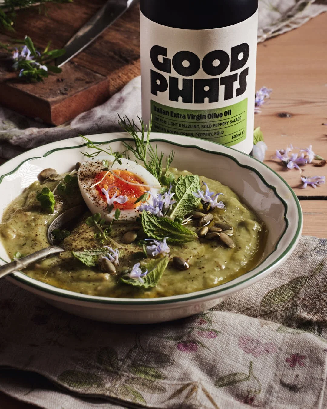 angled image of olive oil being drizzled onto green soup in rustic farmhouse setting