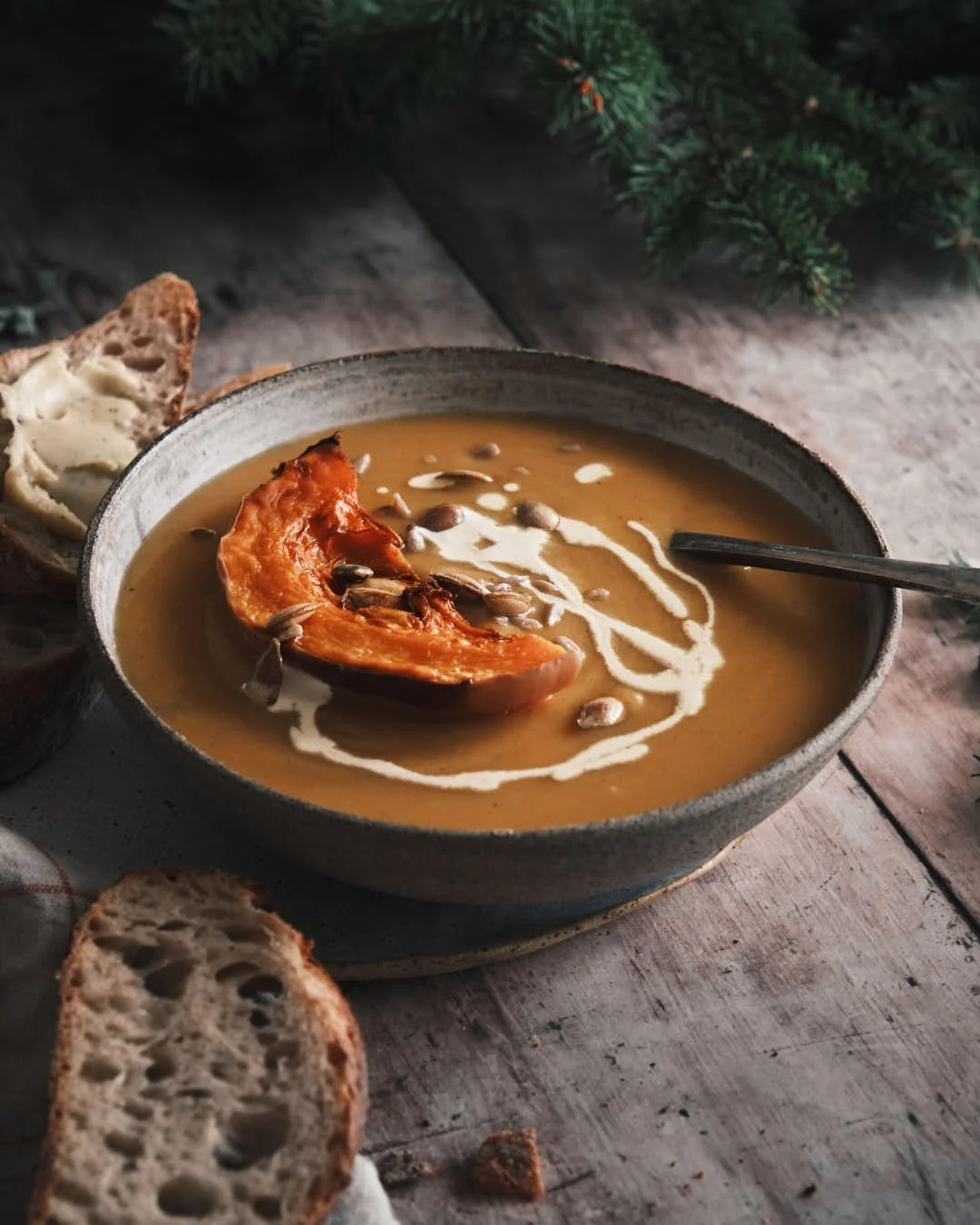angled moody image of butternut squash soup on rustic grey wood background with spruce