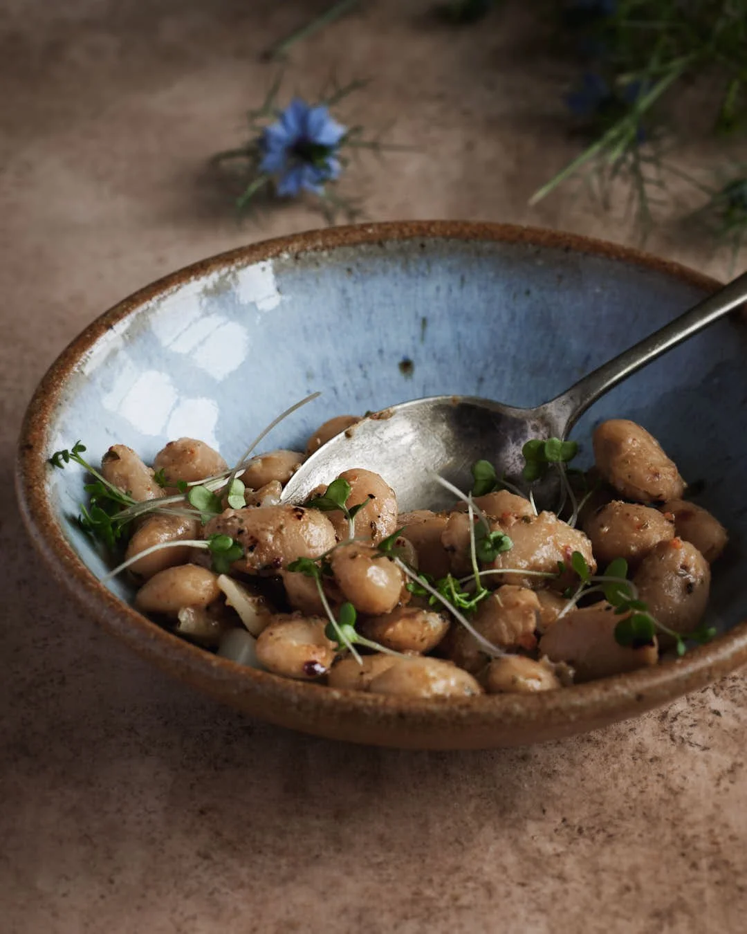 angled image of bowl of butterbeans with herbs on warm hued surface