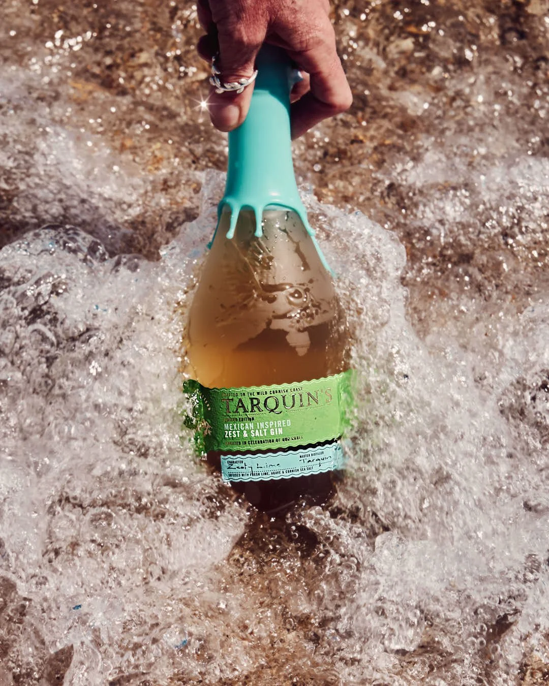 bottle of gin being held in wave of sea