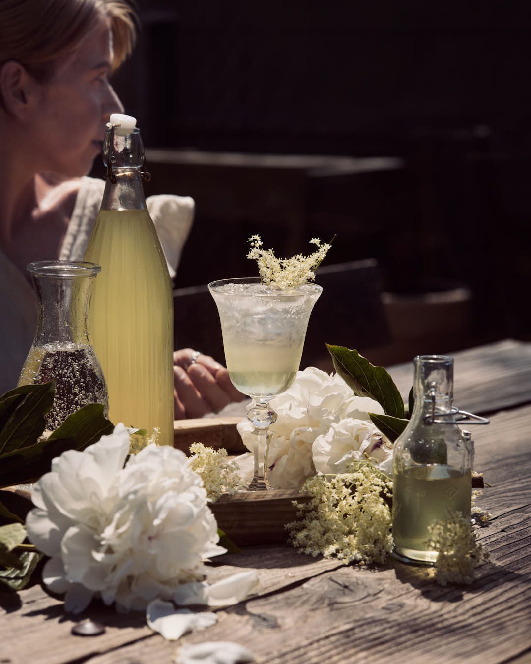 straight on image of girl enjoying elderflower codrial in glass on rustic ourtdoor table