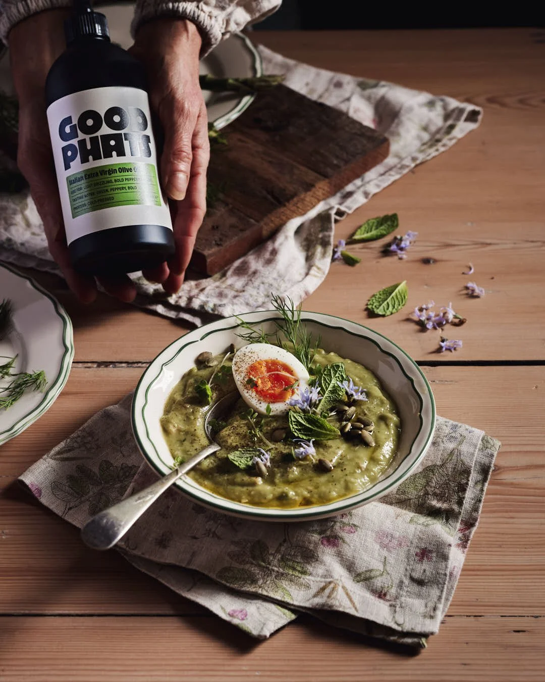 angled image of olive oil being drizzled onto green soup in rustic farmhouse setting