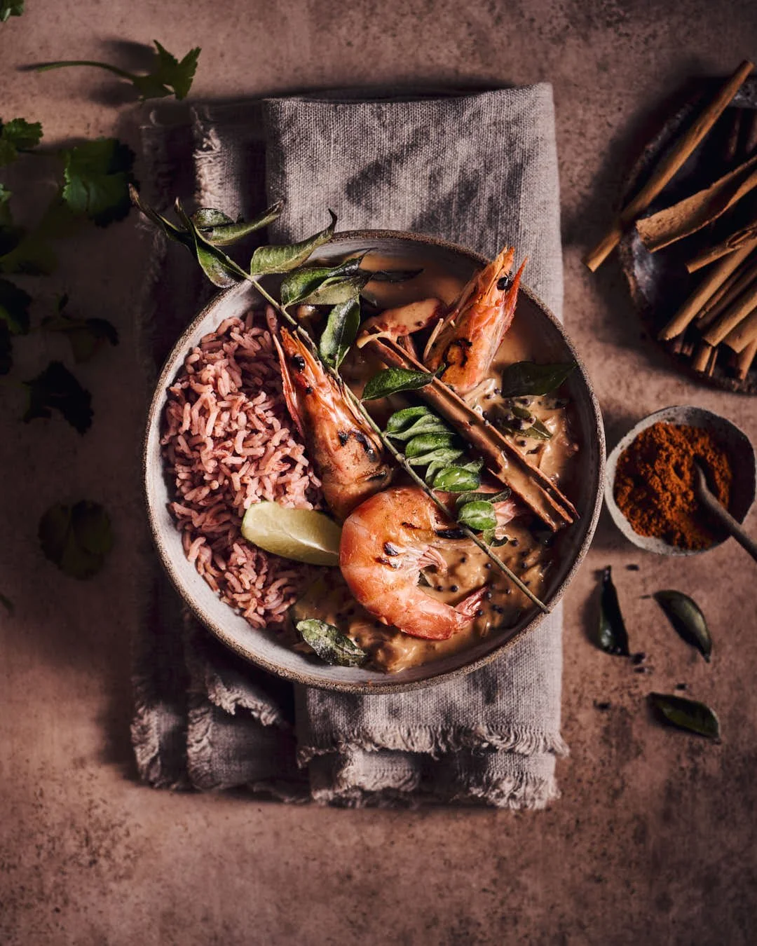 flatlay image of king prawns in curry sauce with toasted curry leaves in dark and moody scene