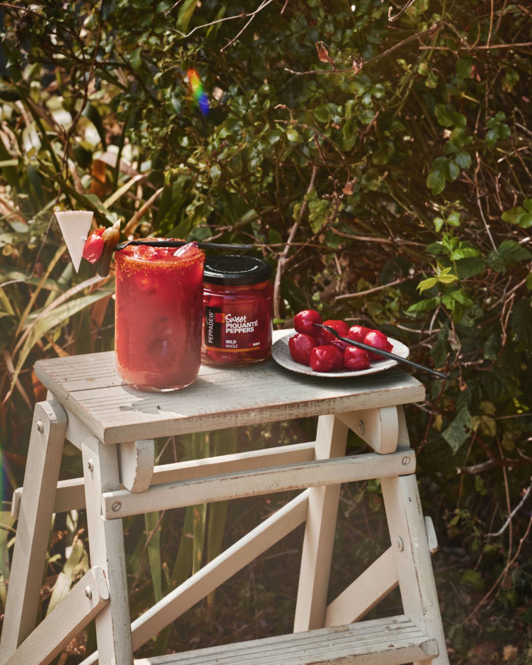 angled image of tomato drink in bright summer sun with gigham dress behind and mini peppers on plate