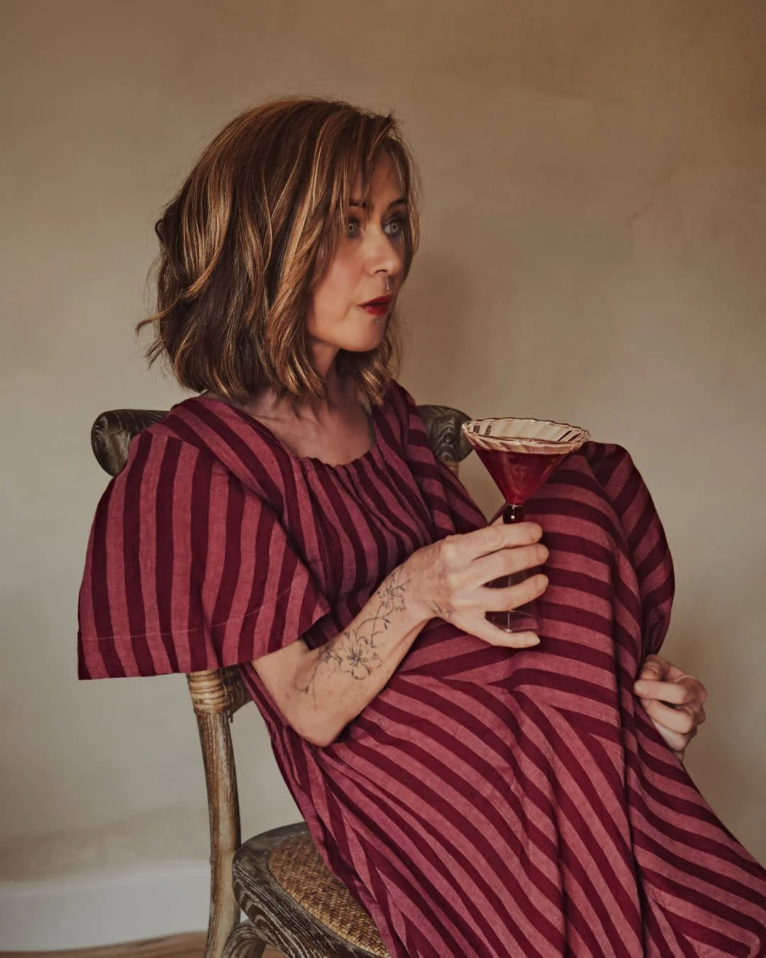 girl with knees at chest on chair in red and pink hued dress holding martini contemplating in stunning vintage scene