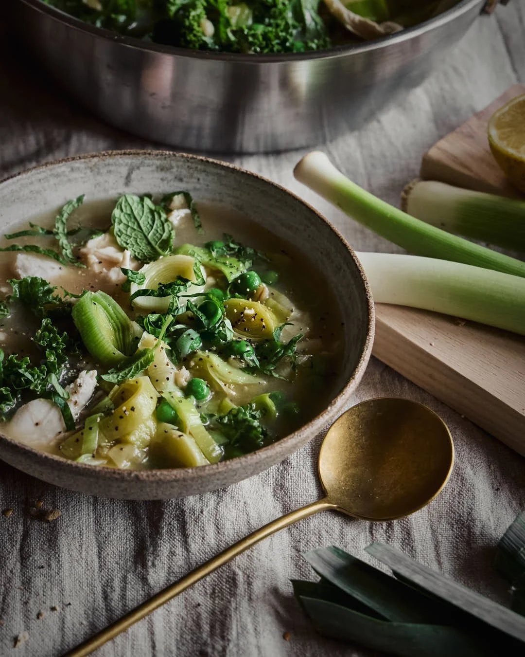 macro image of green vegetable and chicken soup on cool toned linen table cloth