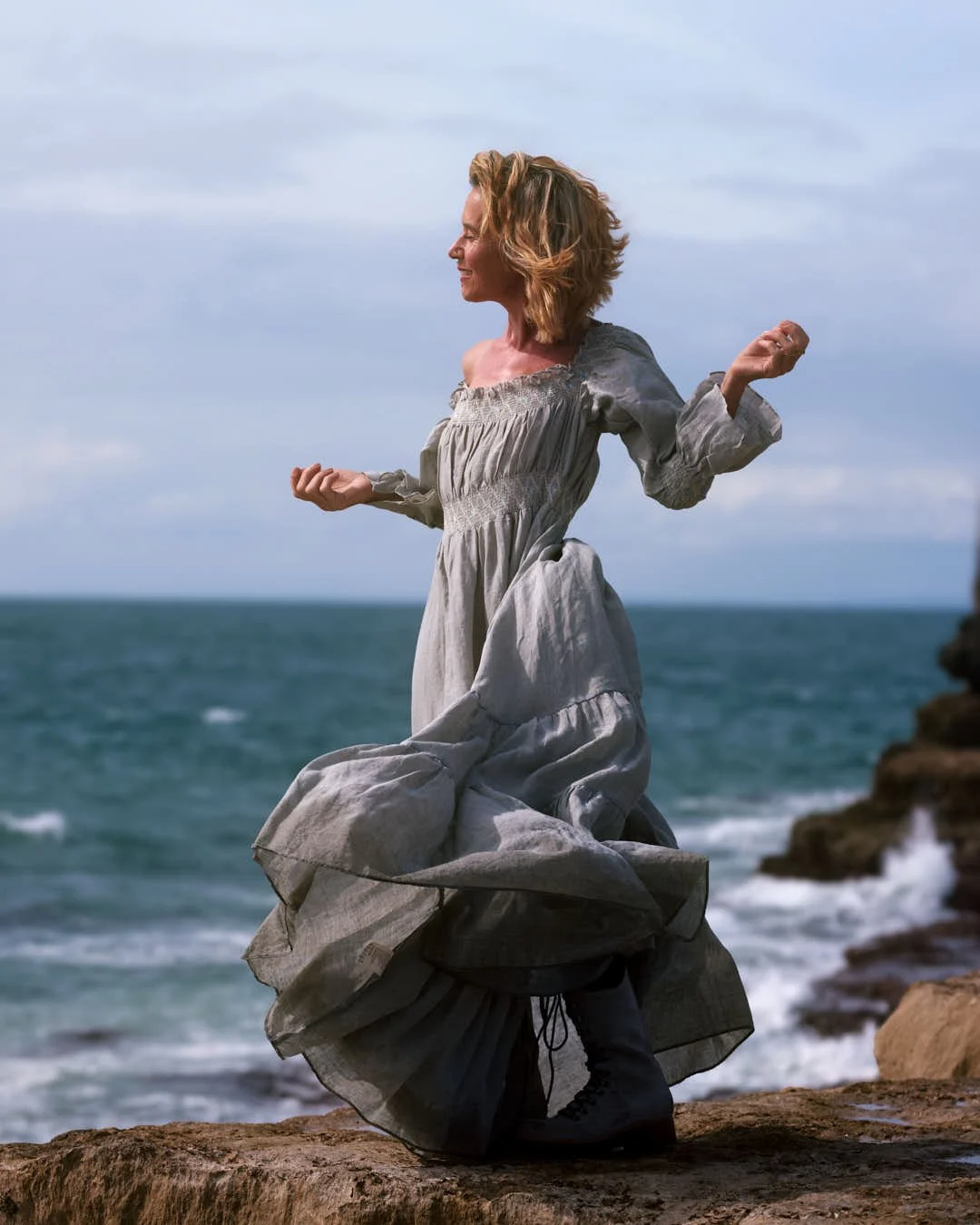 girl on rocks by sea with linen dress blowing in wind