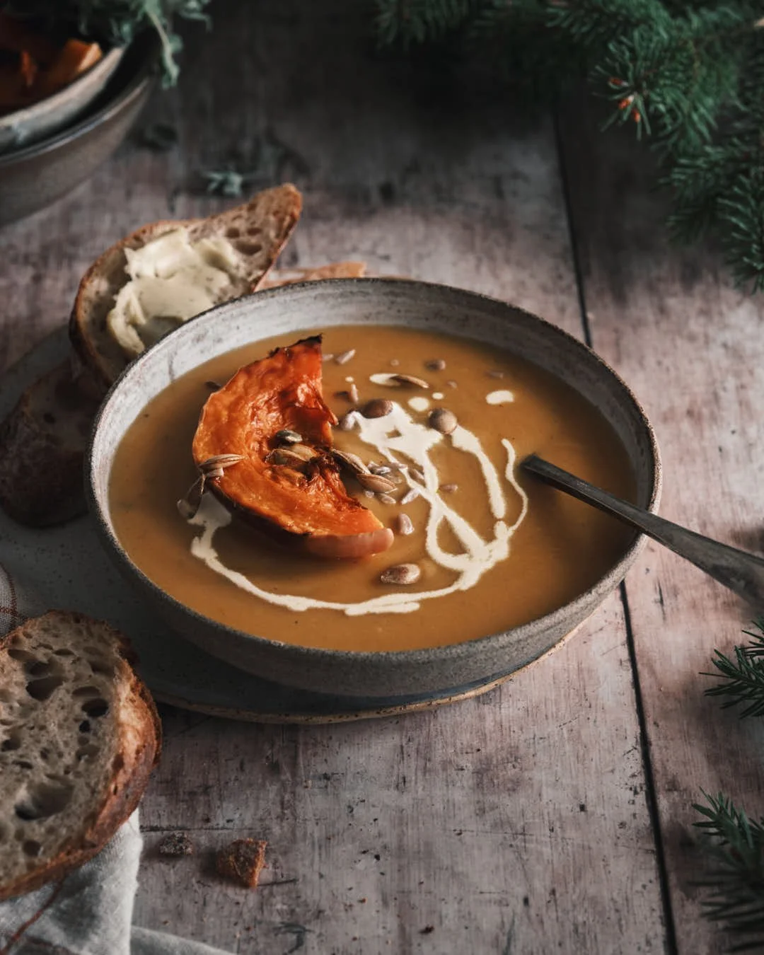 angled moody image of butternut squash soup on rustic grey wood background with spruce
