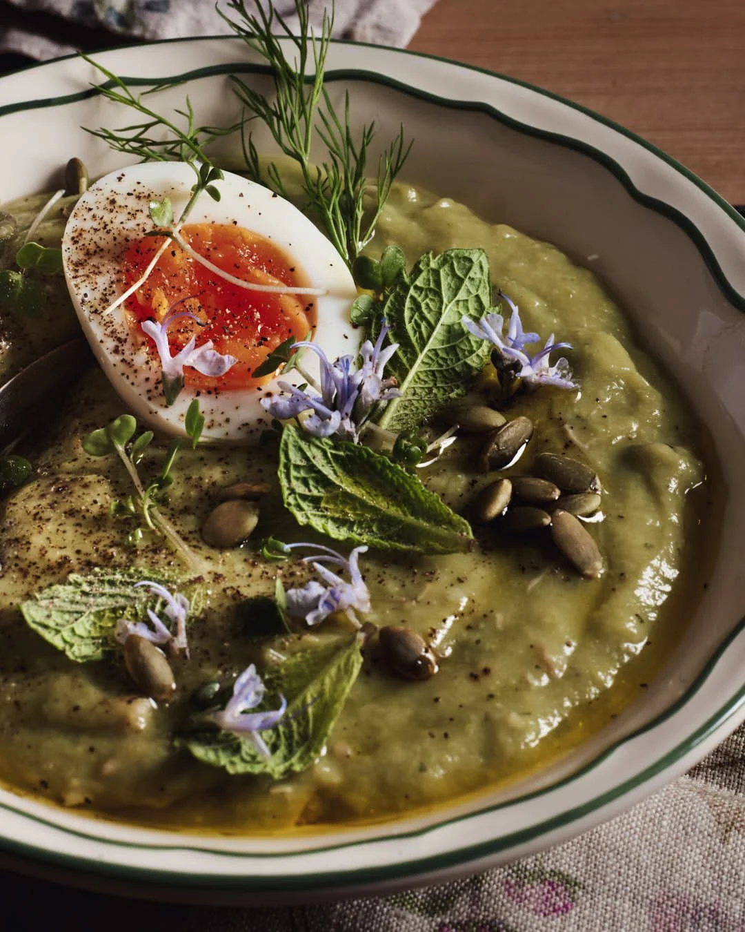 angled image of olive oil being drizzled onto green soup in rustic farmhouse setting