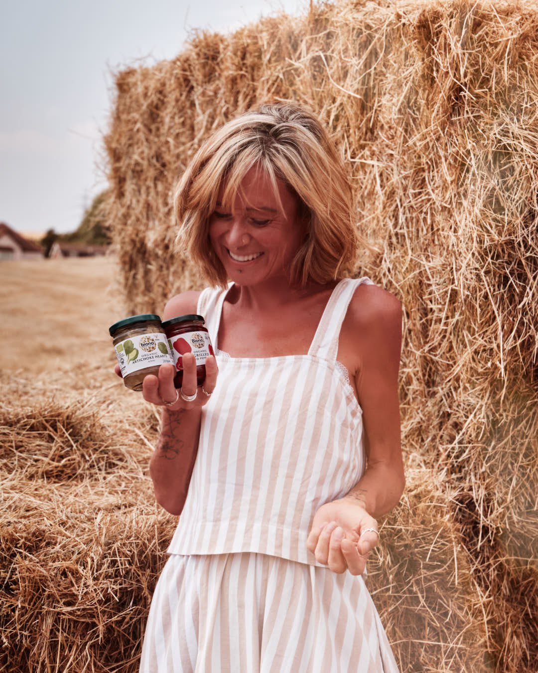 girl holding two jars of anti pasti in front of hay bales in summer shoot