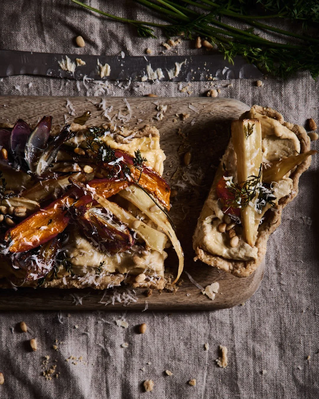 flatlay iage of long tart with hummus and roasted root vegetables in moody winter scene with carrots