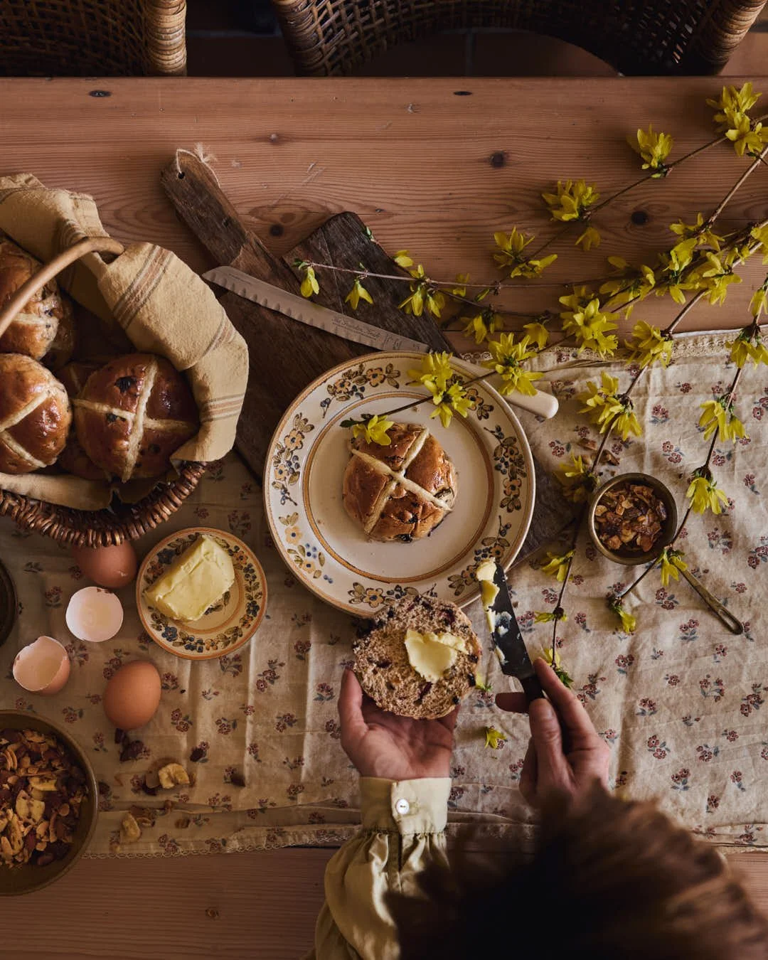 flatlay image of hot cross bun on plate with girl spreading butter